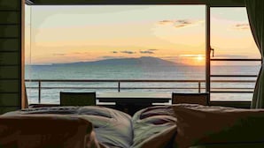 Una habitación con una cama, una mesita y vista al mar al atardecer.