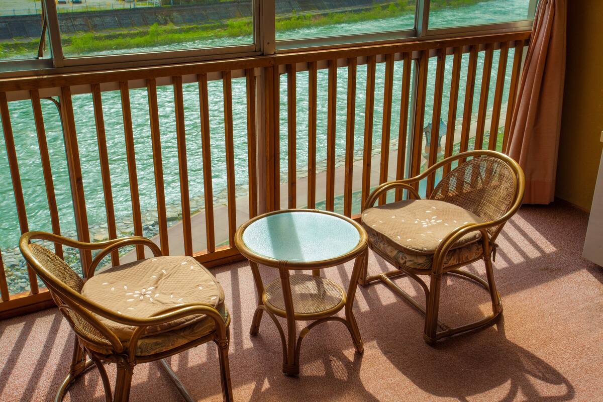 Een balkon met twee rieten stoelen en een tafeltje, met uitzicht op een rivier.