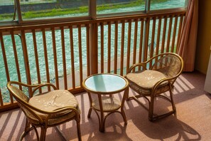 A balcony with two wicker chairs and a small table, overlooking a river.