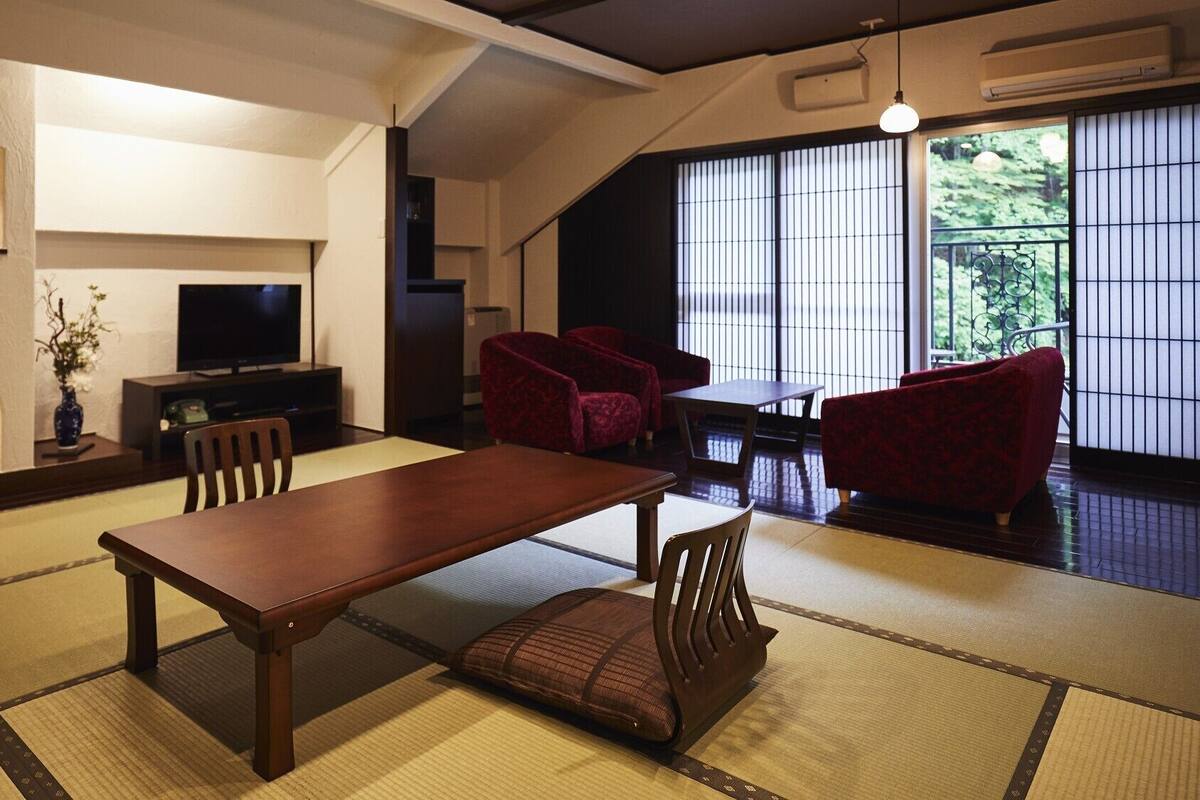 Uma sala de estar tradicional japonesa com tatames, uma mesa baixa e cadeiras vermelhas.