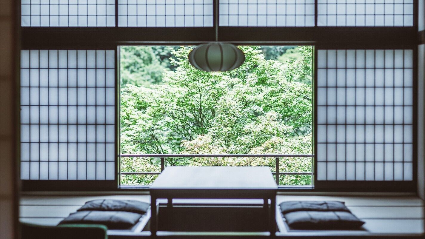 Estada tradicional japonesa amb sòcols de tatami, una taula baixa i vista a un jardí exuberant a través d'una pantalla shoji.
