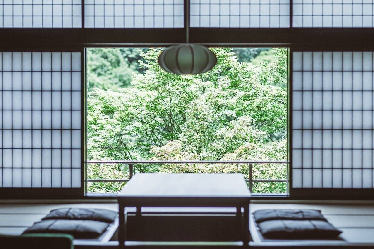 Um quarto japonês tradicional com piso de tatame, uma mesa baixa e vista para um jardim exuberante através de um shoji.