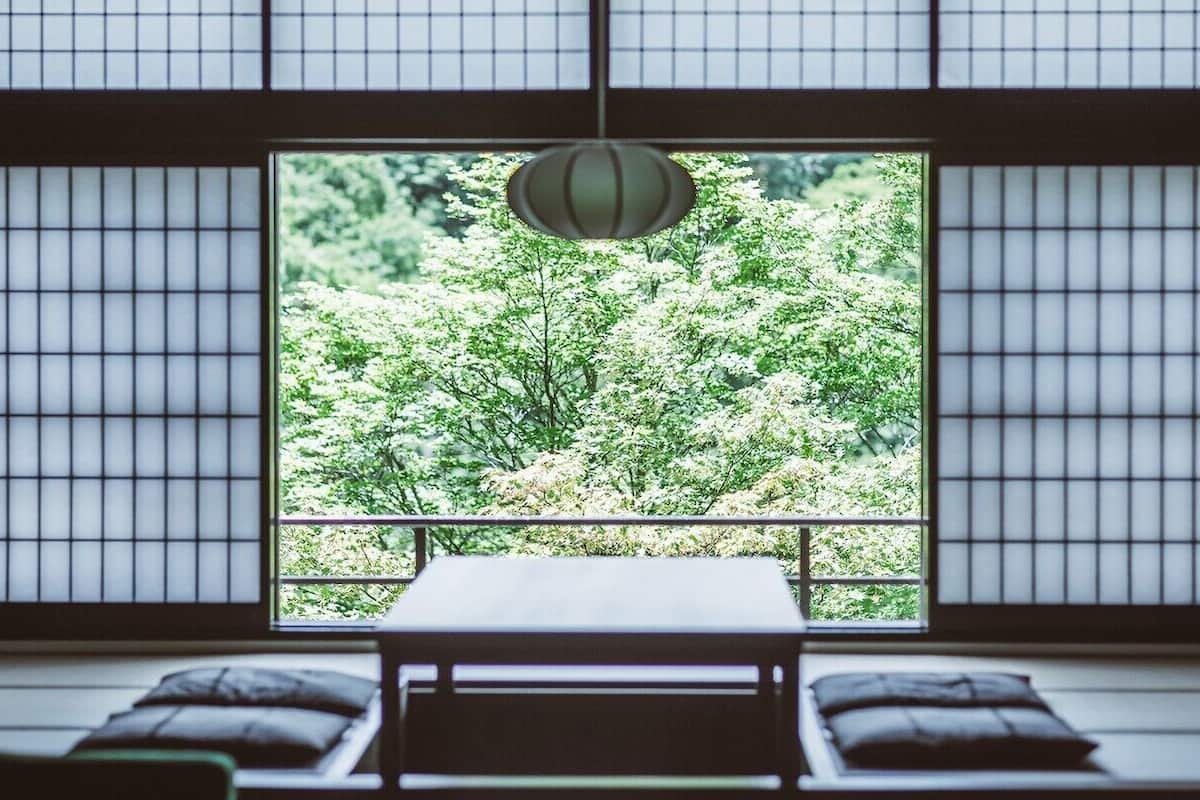 A traditional Japanese room with tatami flooring, a low table, and a view of a lush garden through a shoji screen.