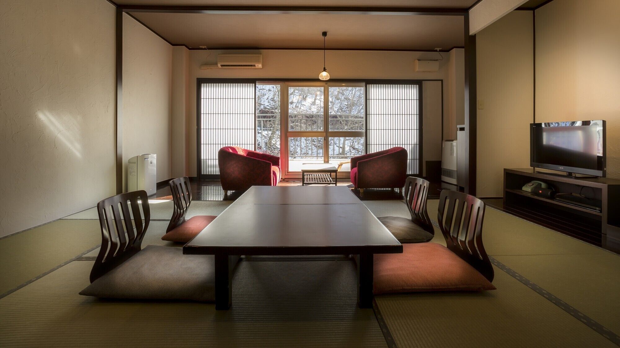 Una habitació tradicional japonesa amb tatami, una taula baixa i cadires amb coixins vermells.