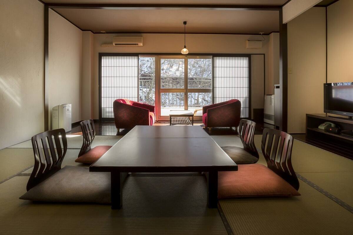 Um quarto em estilo japonês tradicional, com tatames, uma mesa baixa e cadeiras almofadadas vermelhas.