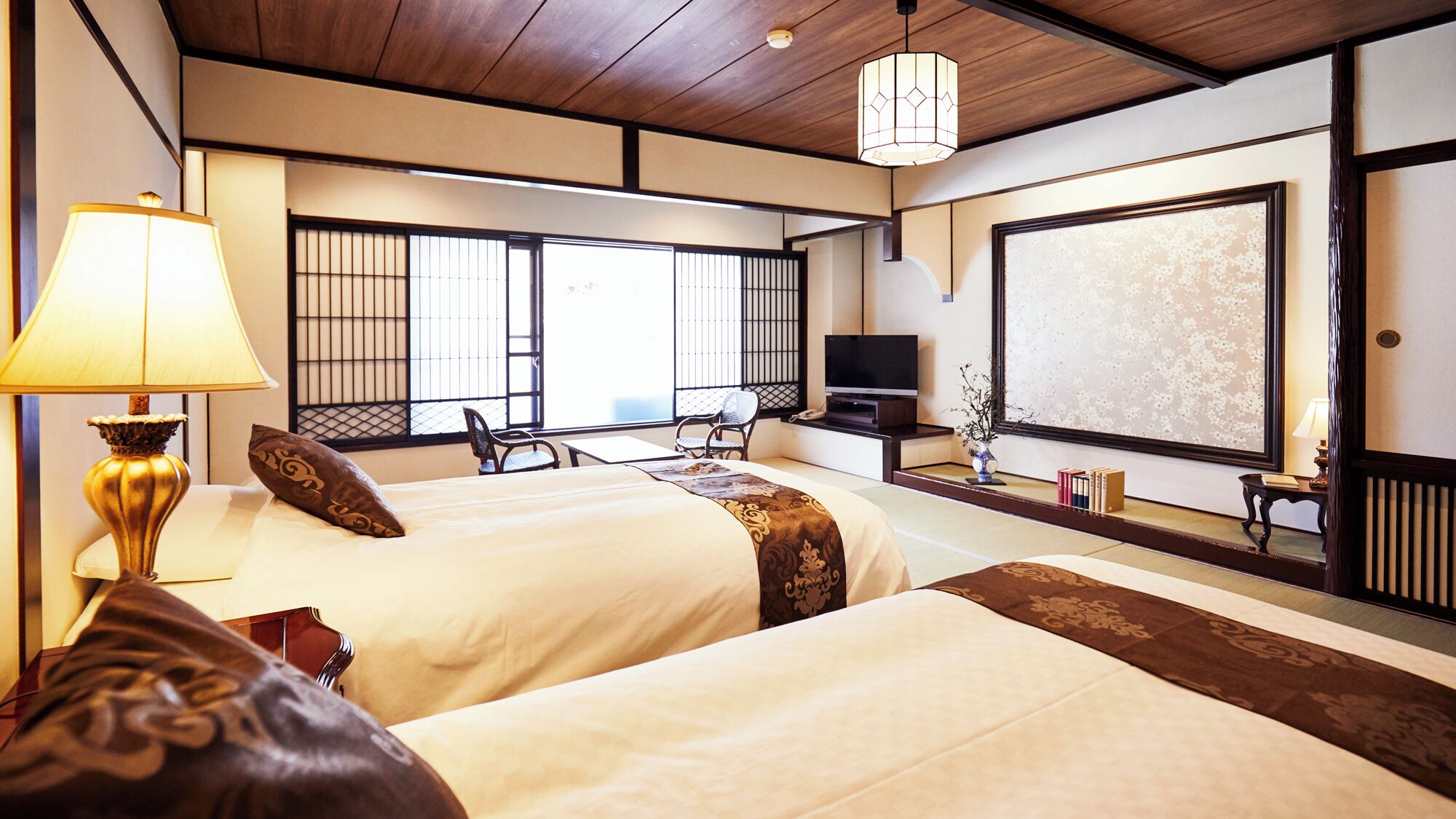 A hotel room with two beds, a TV, a desk, and a view of the outside.