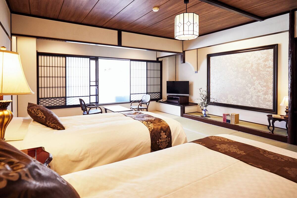 Quarto de hotel com duas camas, televisão, escrivaninha e vista para o exterior.