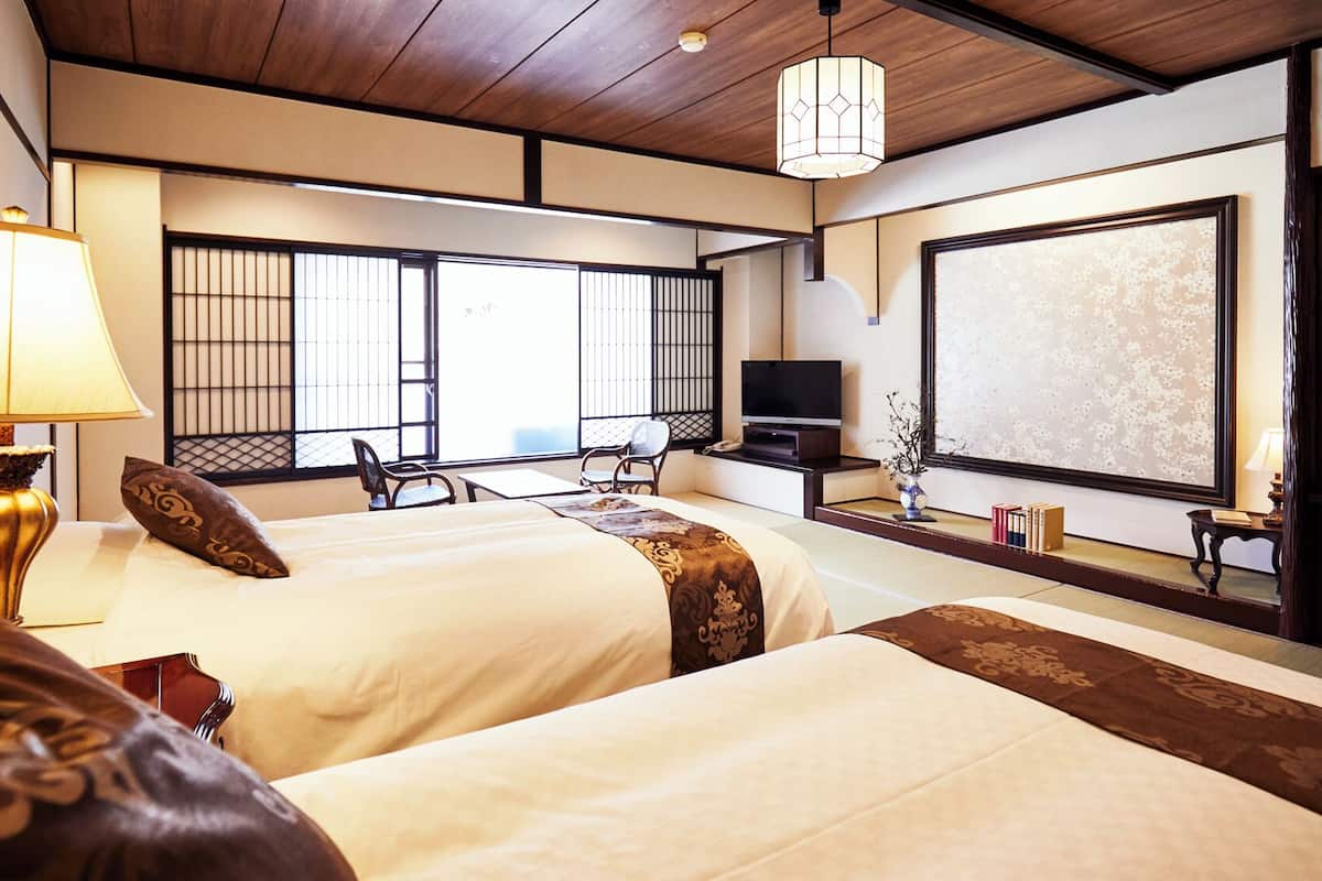 A hotel room with two beds, a TV, a desk, and a view of the outside.