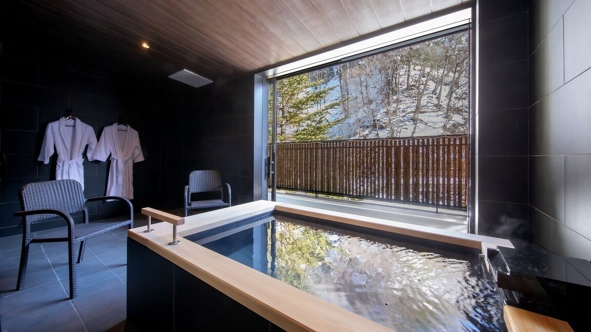 Una habitació d'spa moderna amb una finestra gran, una banyera hidromassatge i dues robes blanques penjades en un suport.
