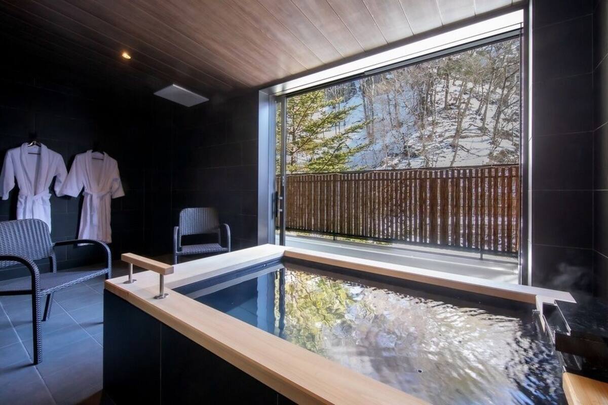 Uma sala de spa moderna com uma janela ampla, uma banheira de hidromassagem e dois roupões brancos em um suporte.