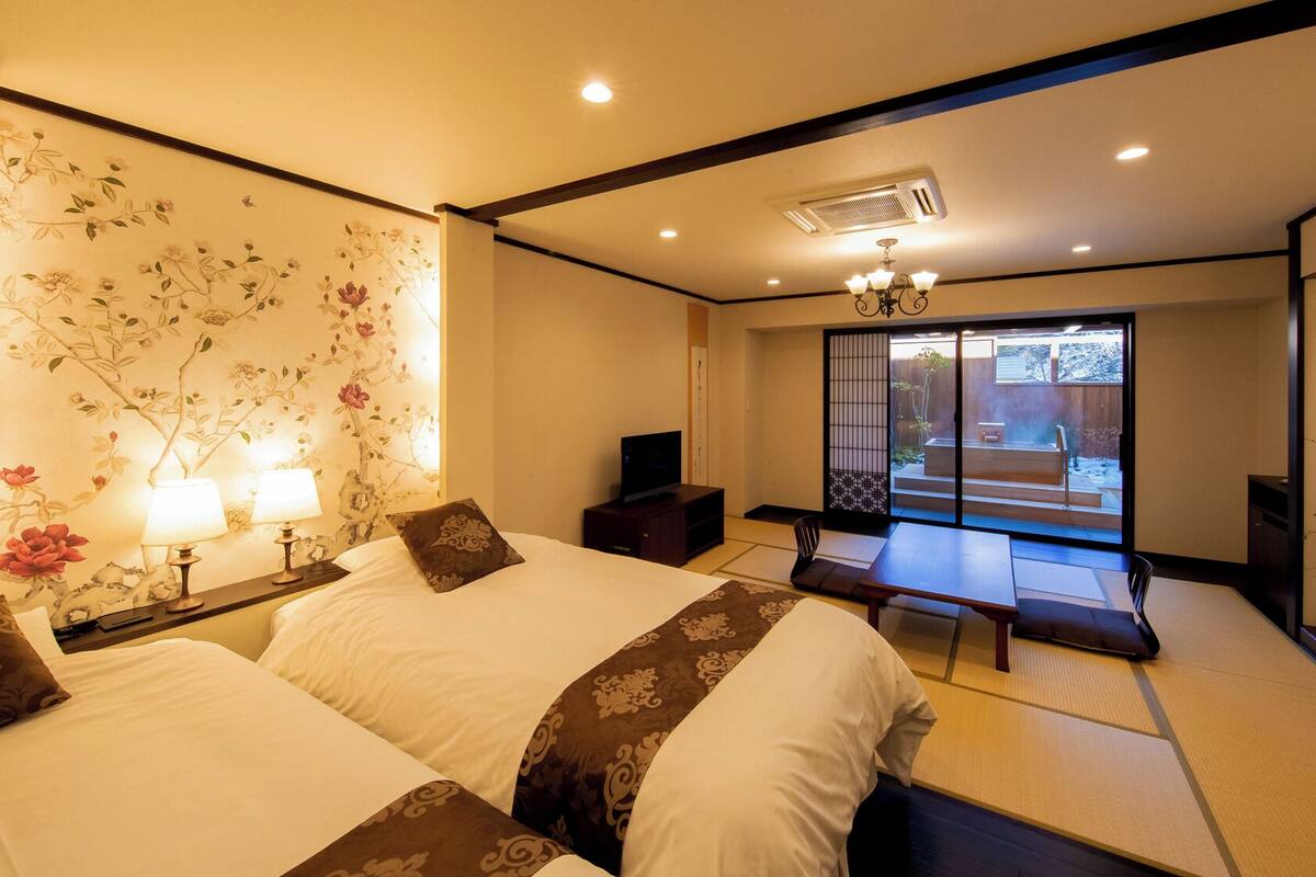 Quarto tradicional japonês, com piso de tatame, porta deslizante para uma varanda e uma televisão sobre uma mesinha.