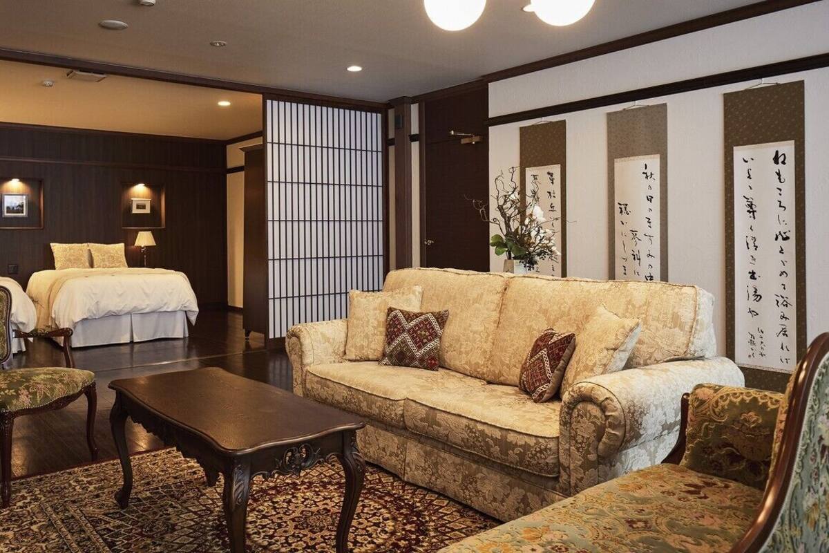 Quarto de hotel com sofá, duas cadeiras, mesa de centro e cama.