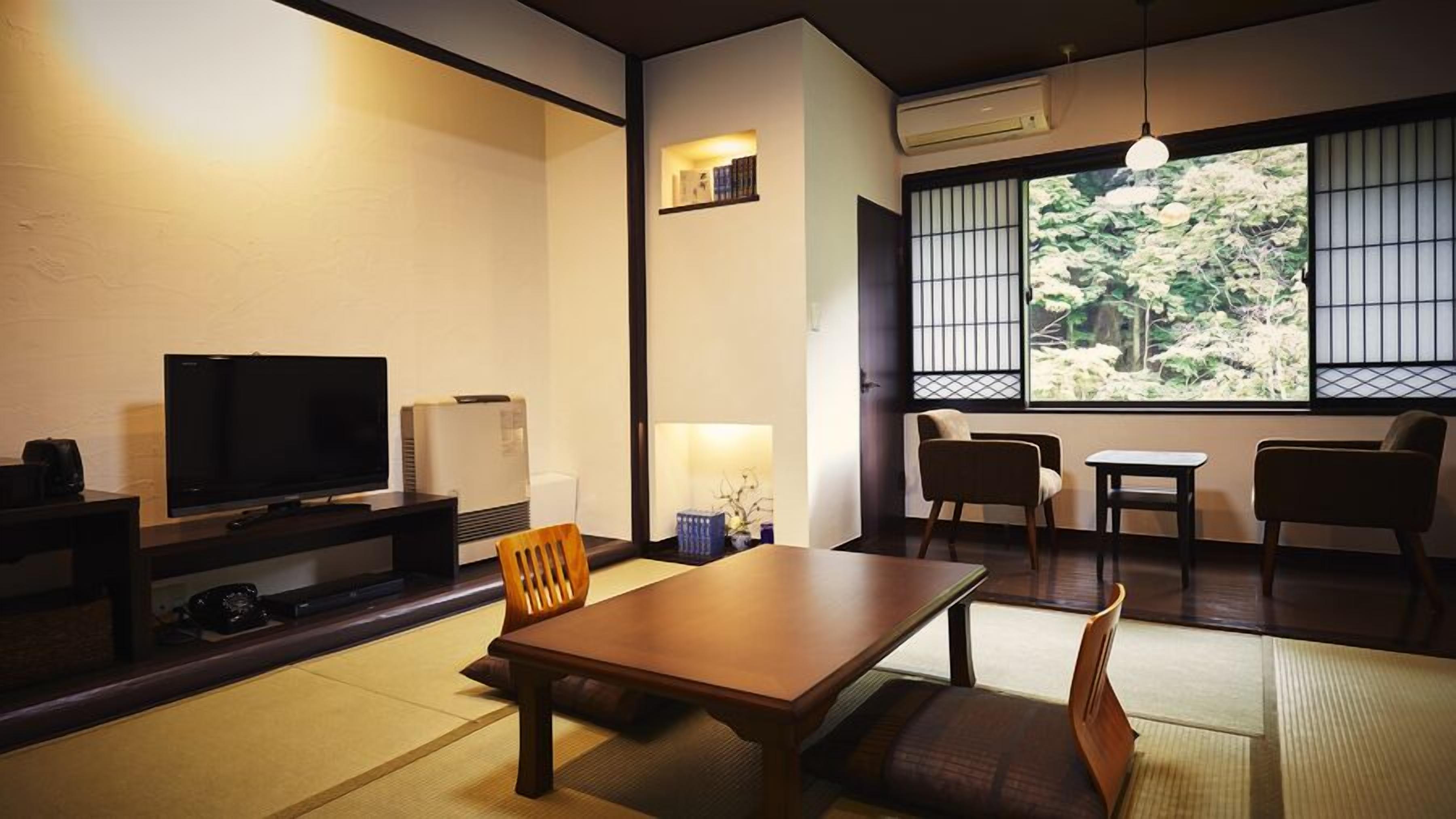 Habitació tradicional japonesa amb fons de tatami, televisió, calefacció i vista a arbres a través d'una pantalla shoji.