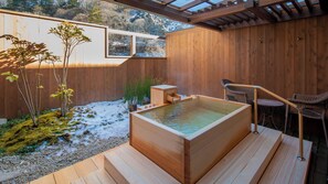 Una terraza de madera con un jacuzzi, asientos al aire libre y vistas a un paisaje nevado.