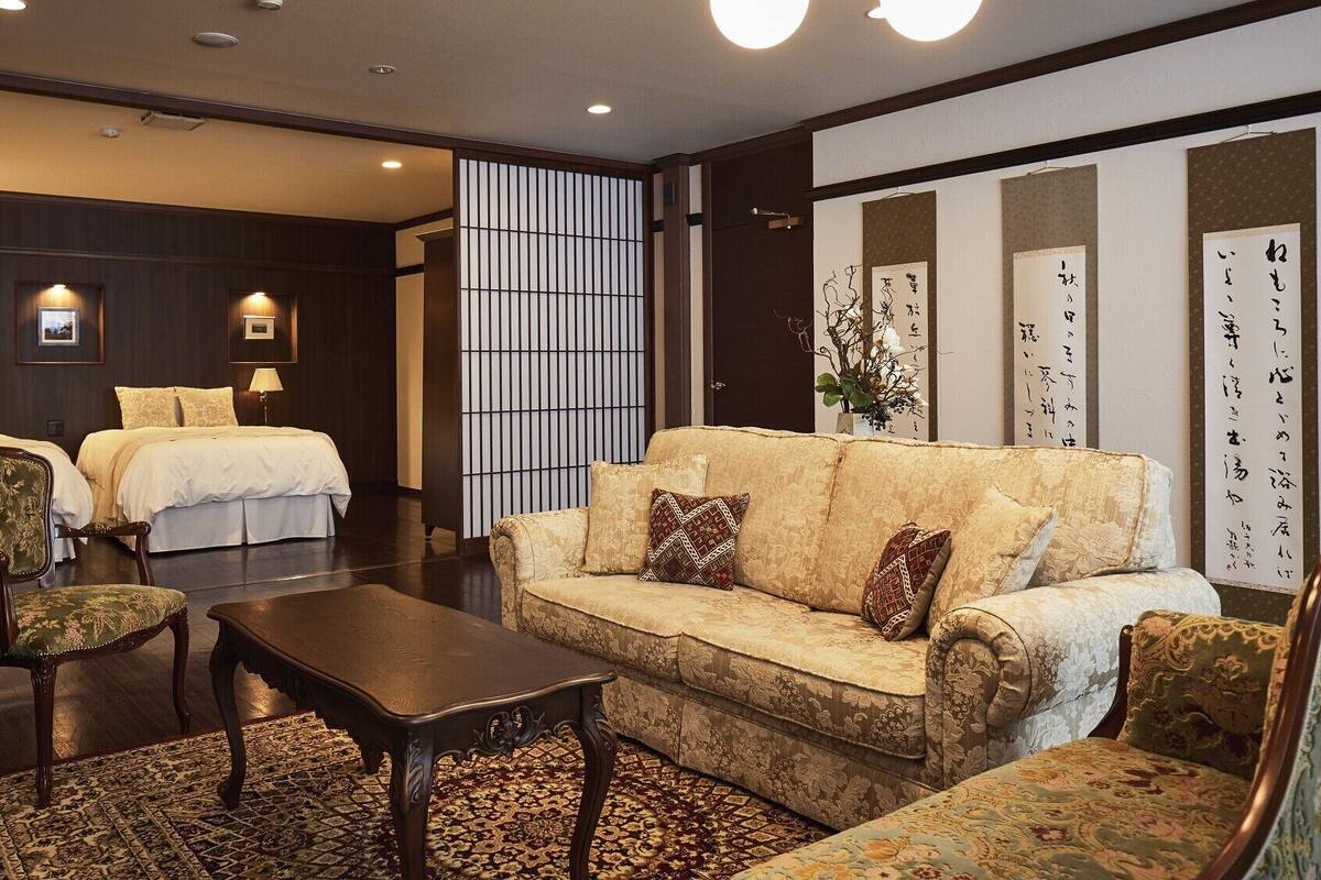 Quarto de hotel com sofá, cadeiras, mesa e duas camas.