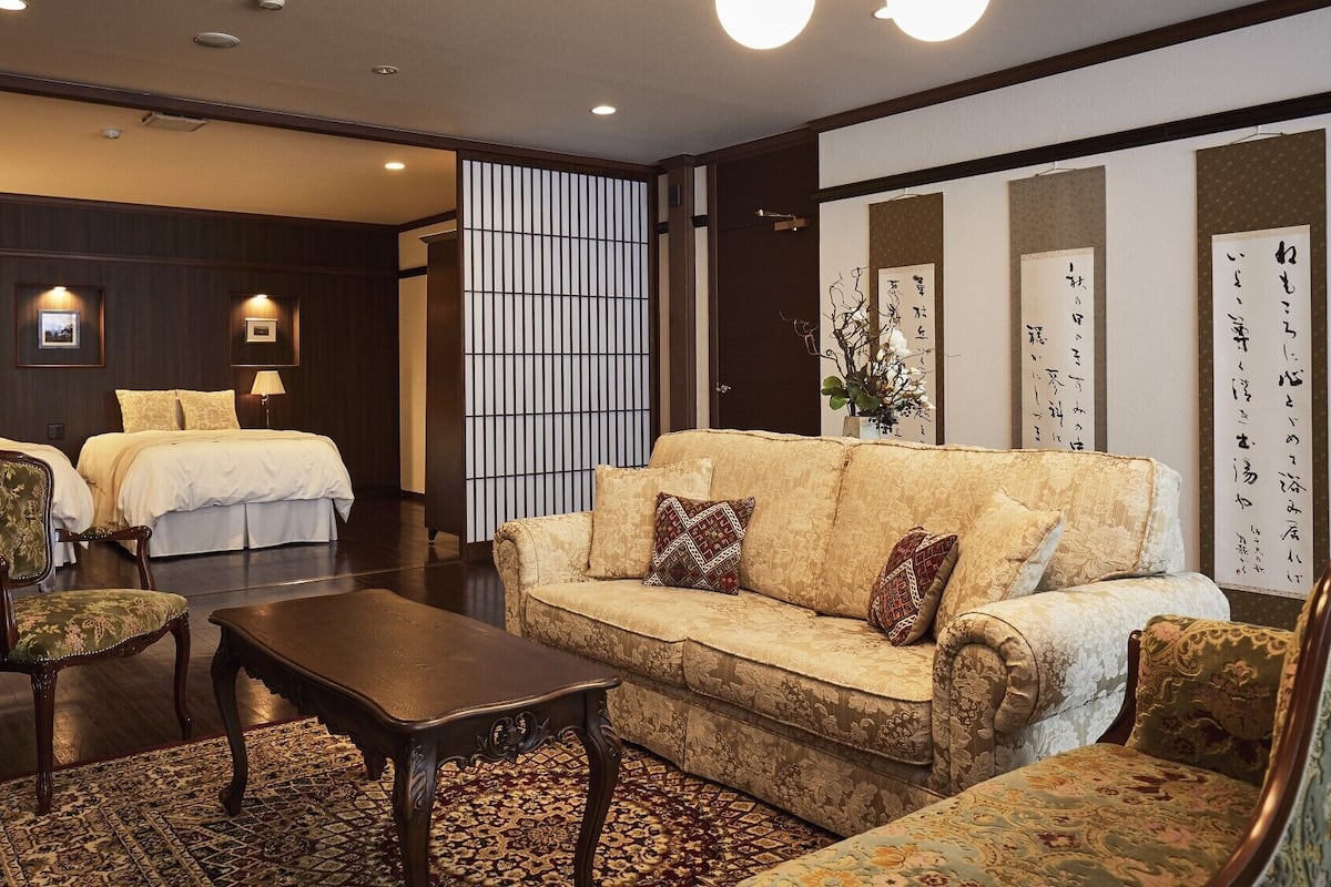 A hotel room with a sofa, chairs, a table, and two beds.