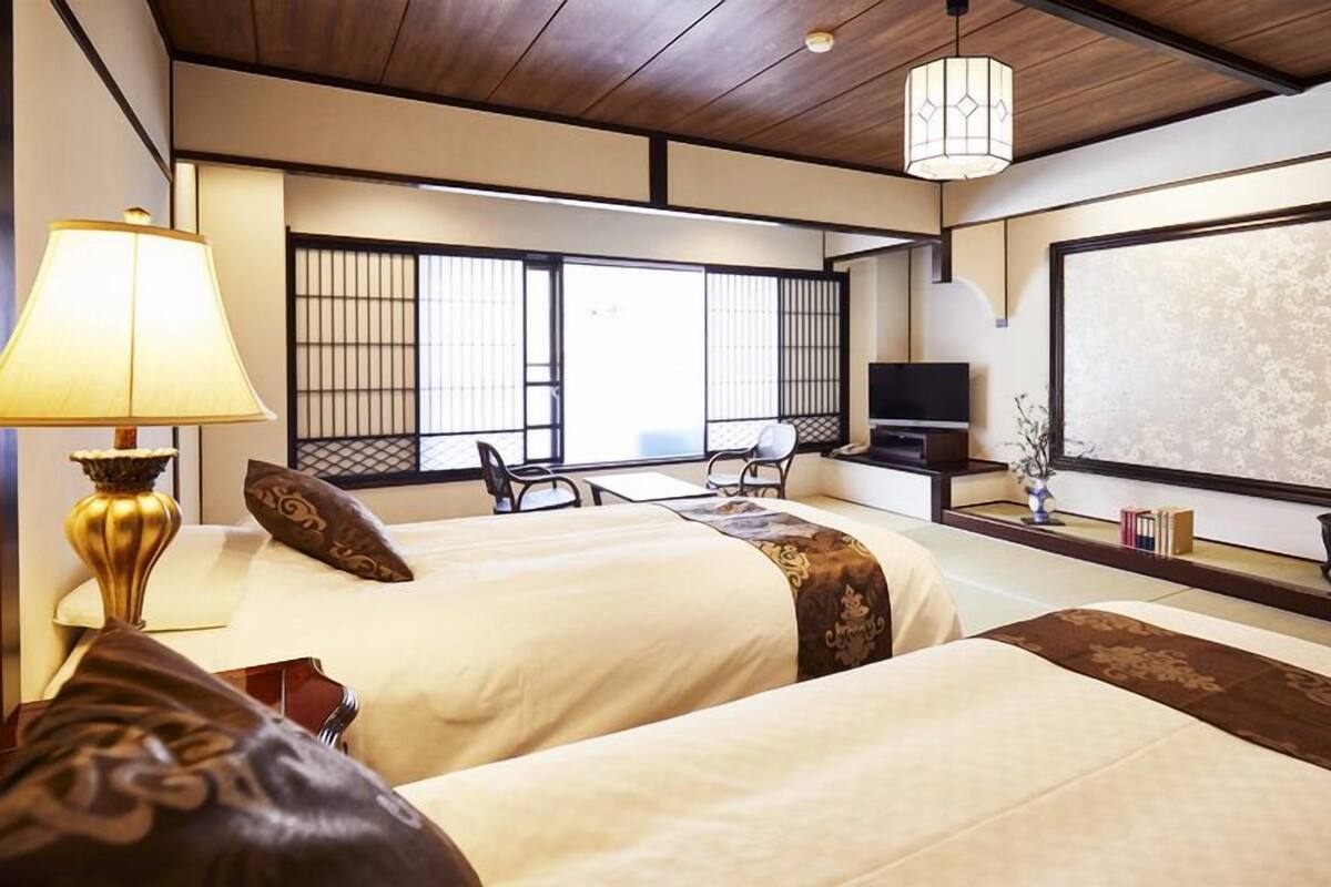 Quarto de hotel com duas camas, televisão, escrivaninha e uma janela grande.
