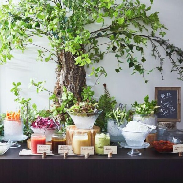 Una mesa de buffet con diversos alimentos y una planta de interior grande.