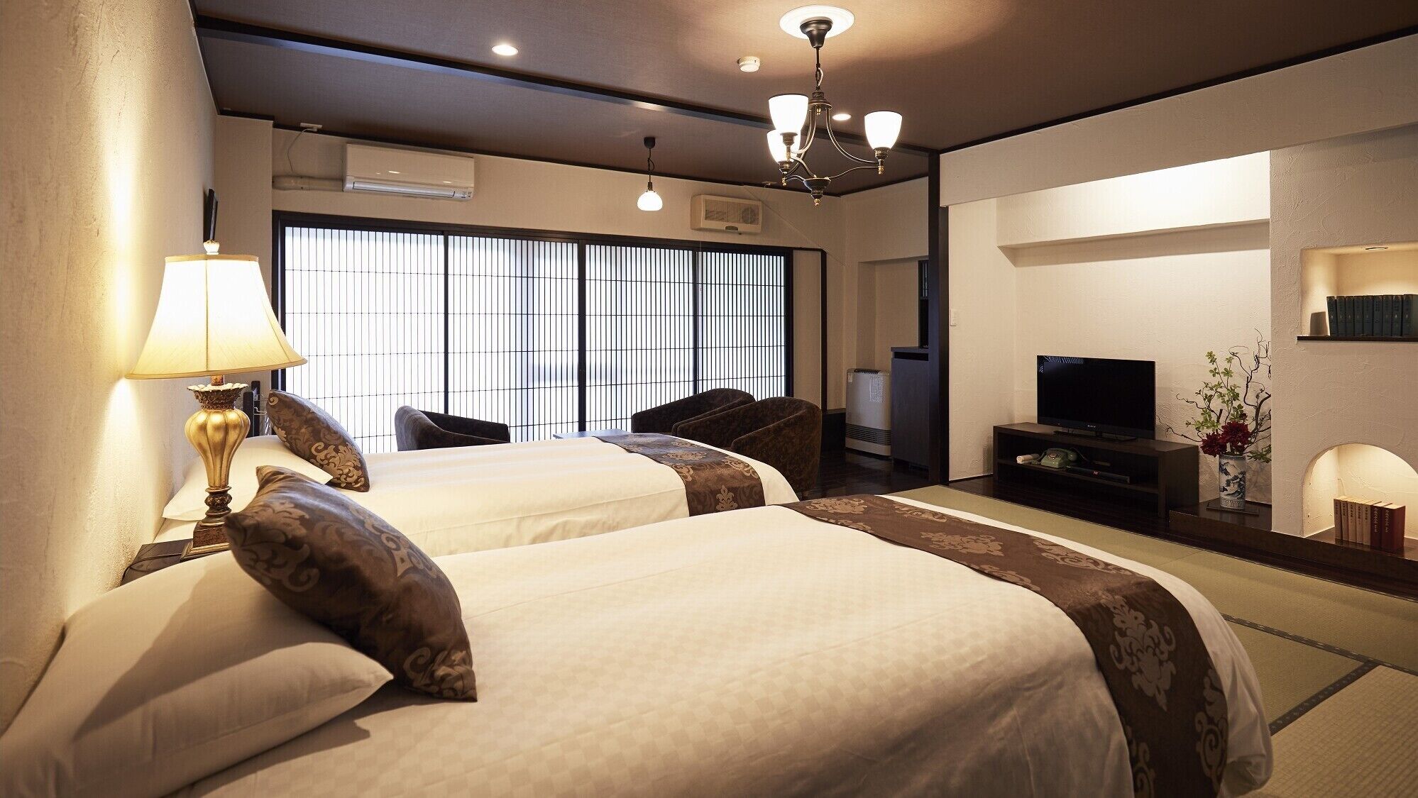A hotel room with two beds, a TV, a bookshelf, and a mirror.