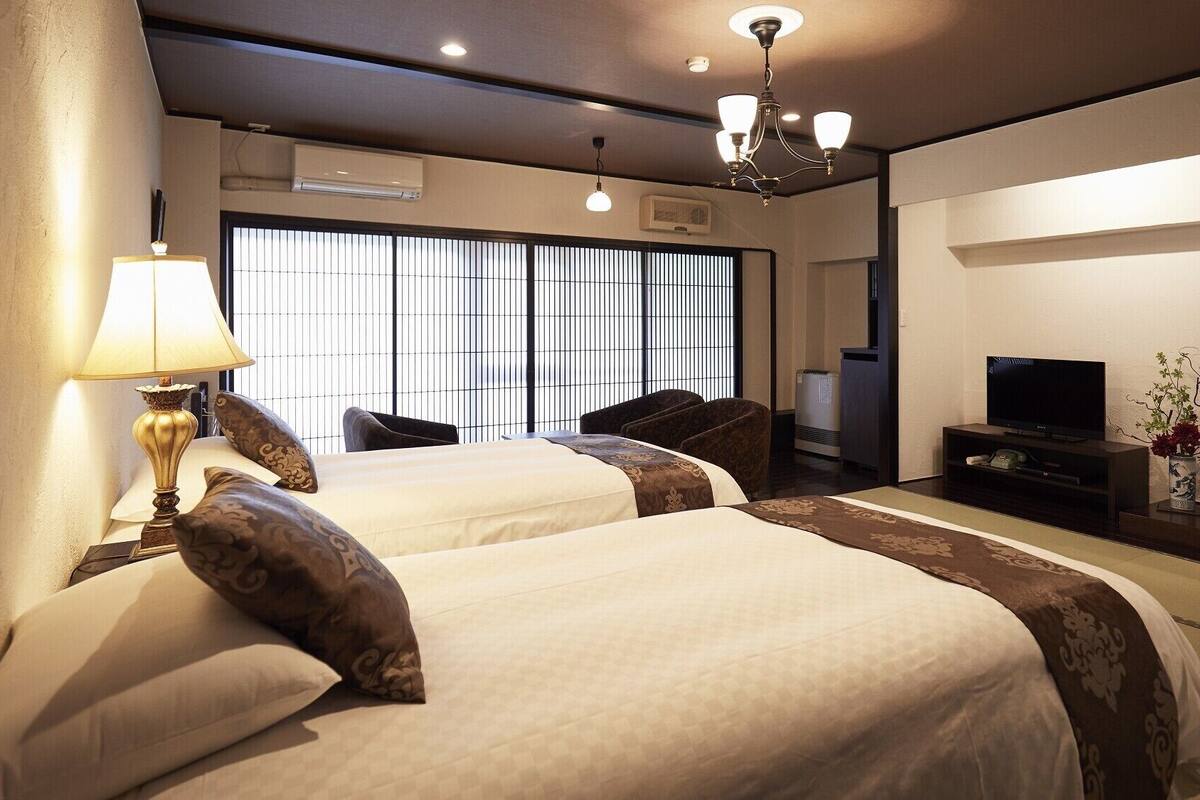 Quarto de hotel com duas camas, televisão, estante de livros e espelho.