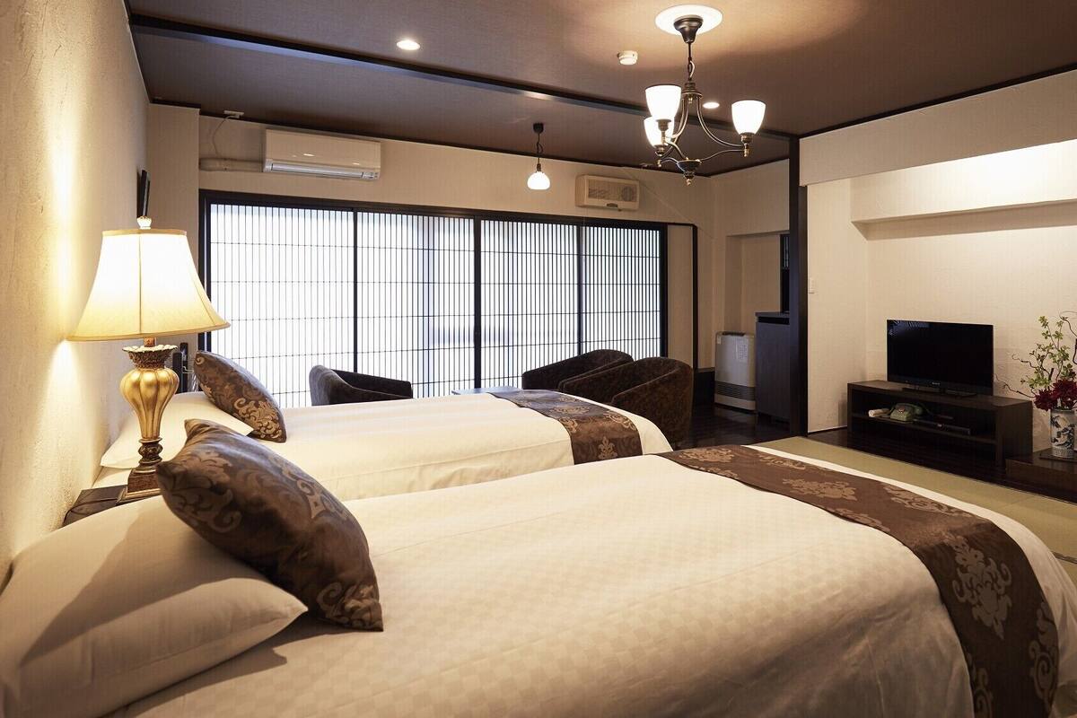 Quarto de hotel com duas camas, uma televisão, uma estante e um espelho.
