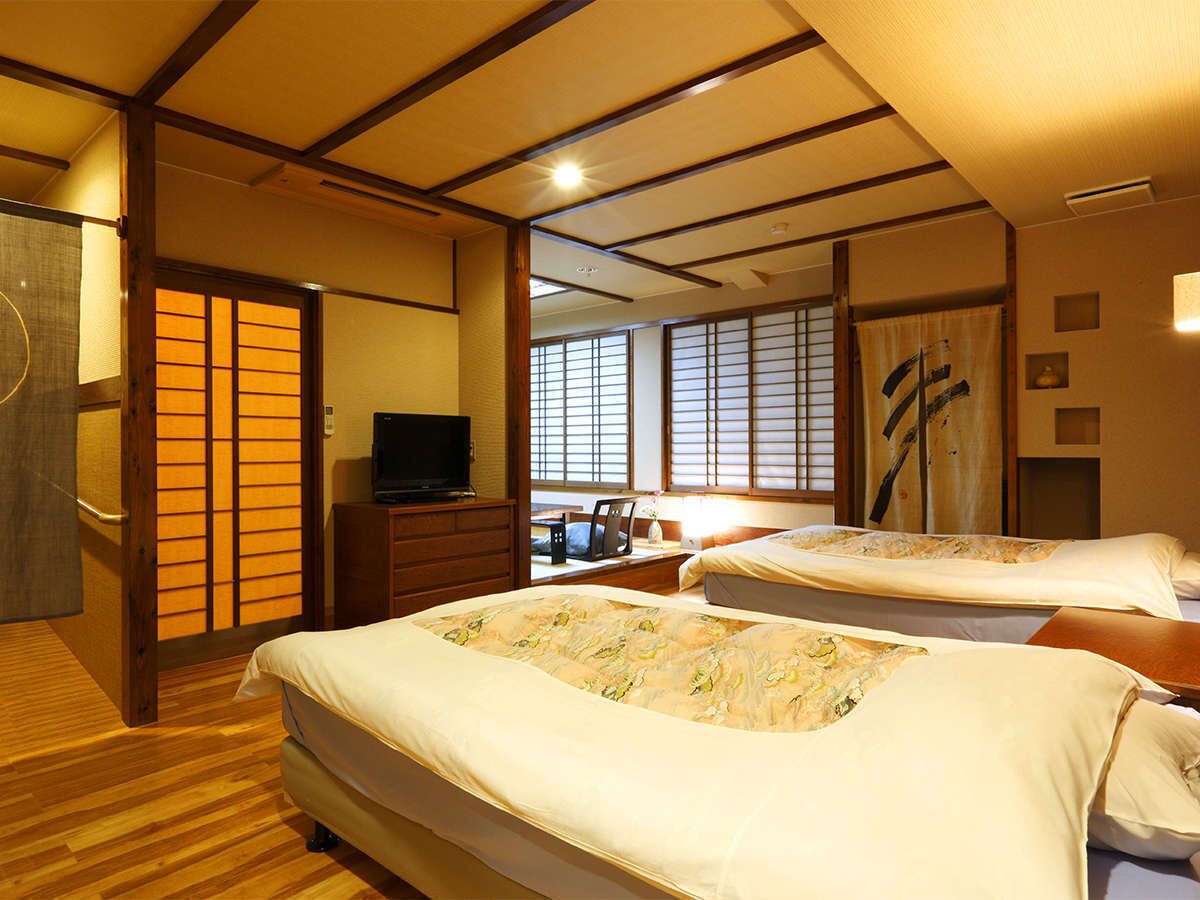 Quarto de hotel em estilo japonês tradicional, com tatames, duas camas, uma televisão e portas deslizantes.