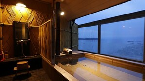 A room with a large window overlooking a body of water, a wooden interior, and a bathtub. - Tokiwaya (Numazu)