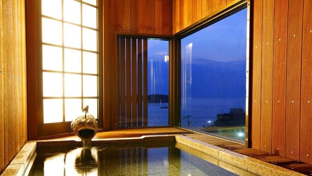 A traditional Japanese onsen with wooden walls and a large window overlooking a body of water. - Tokiwaya (Numazu)
