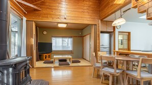 A cozy room with a wooden ceiling, a television, a dining table with chairs, a sofa, and a fireplace. - YATSUGATAKE KOGEN RESORT (Hokuto)