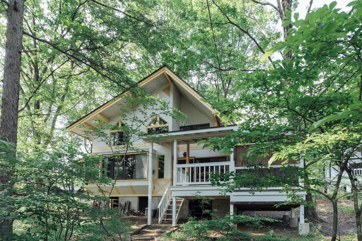 A two-story cabin surrounded by dense forest.