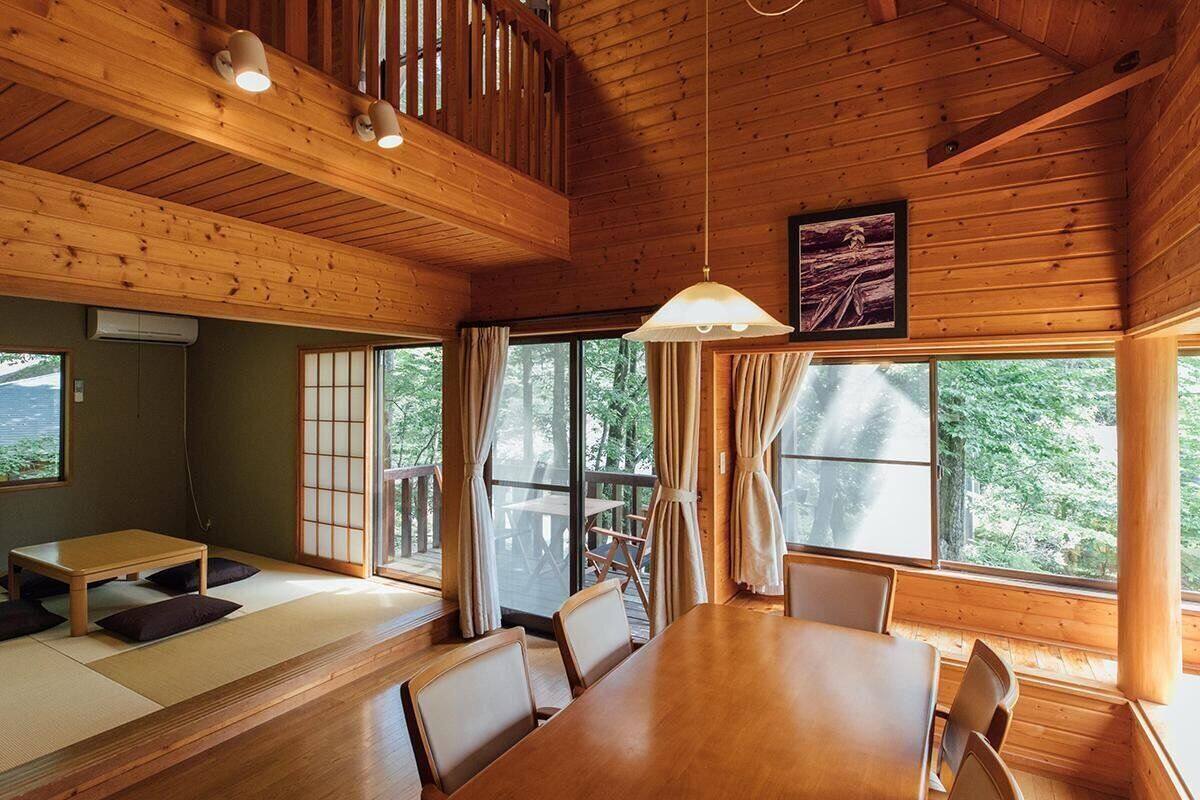 A traditional Japanese-style room with tatami flooring, a wooden dining table, and large windows offering a view of the outdoors.