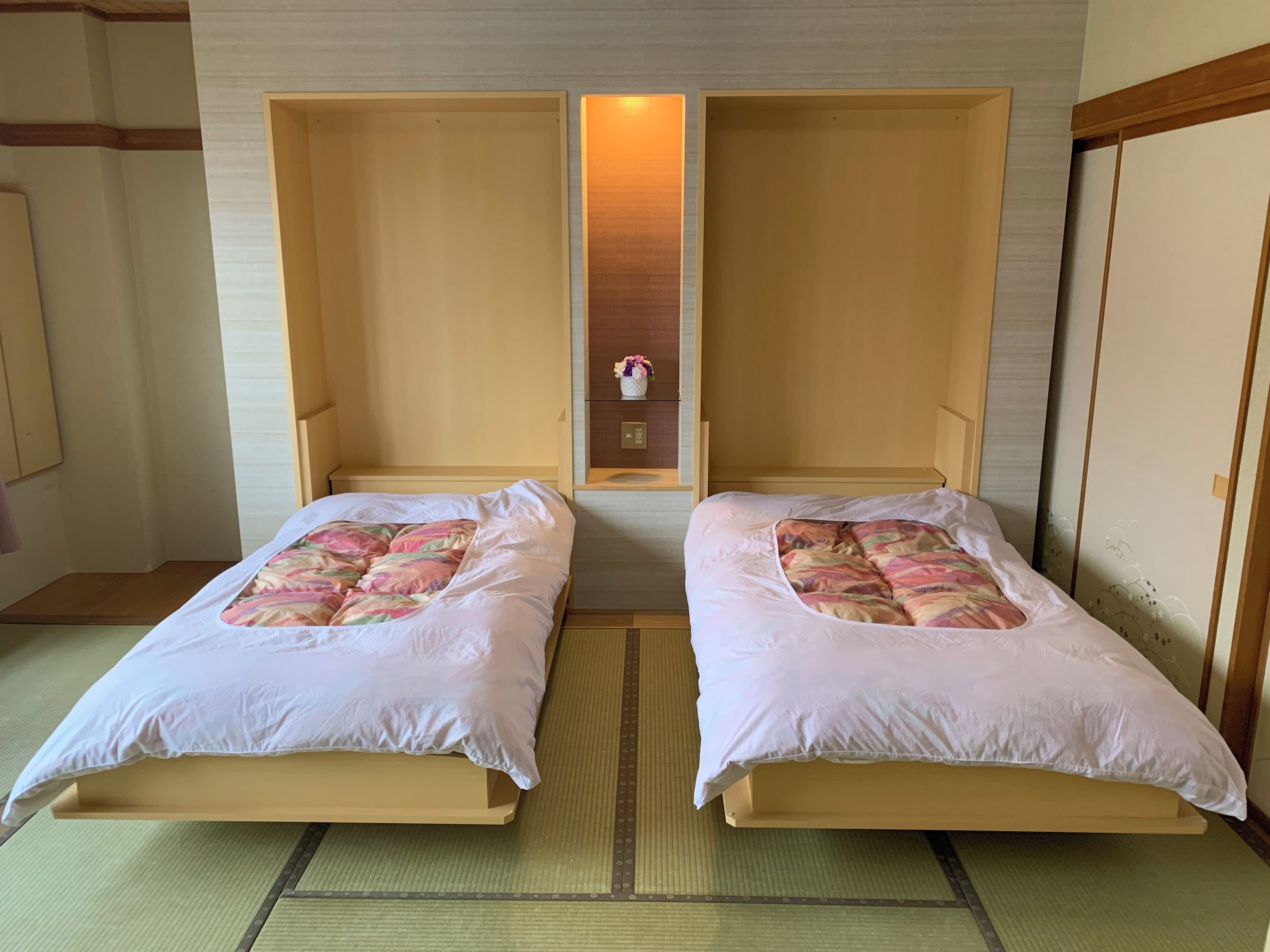 A room with two beds, a small shelf with flowers, and a sliding door.
