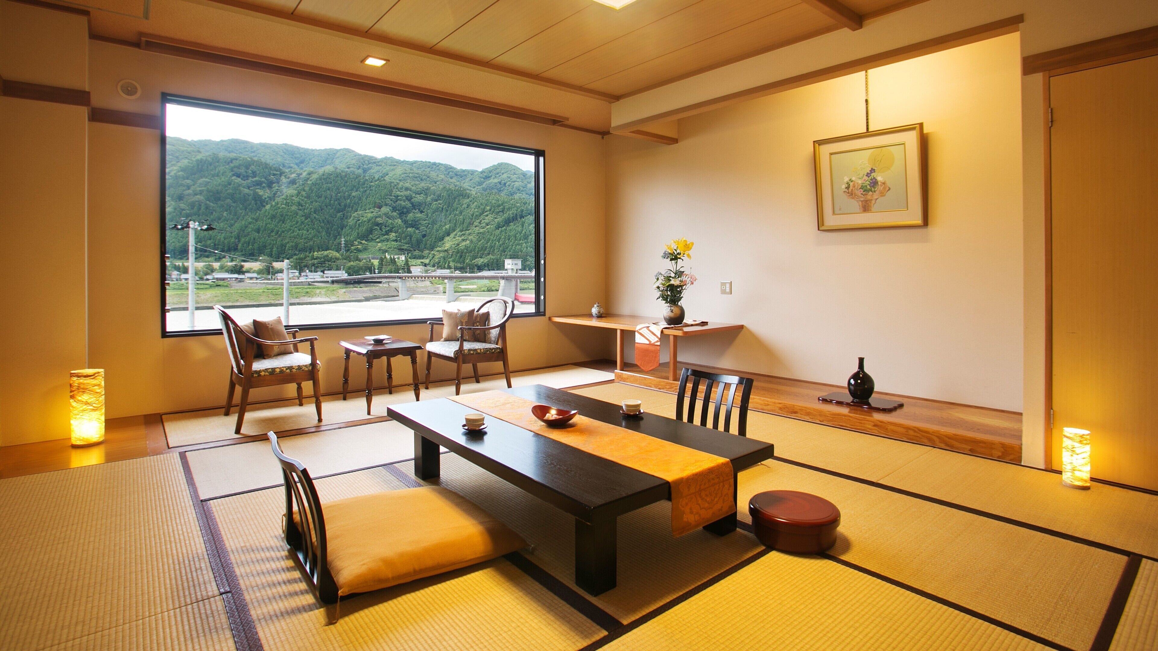 Una habitació tradicional japonesa amb sòls de tatami, una taula baixa, cadires, vista a les muntanyes i un quadre a la paret.