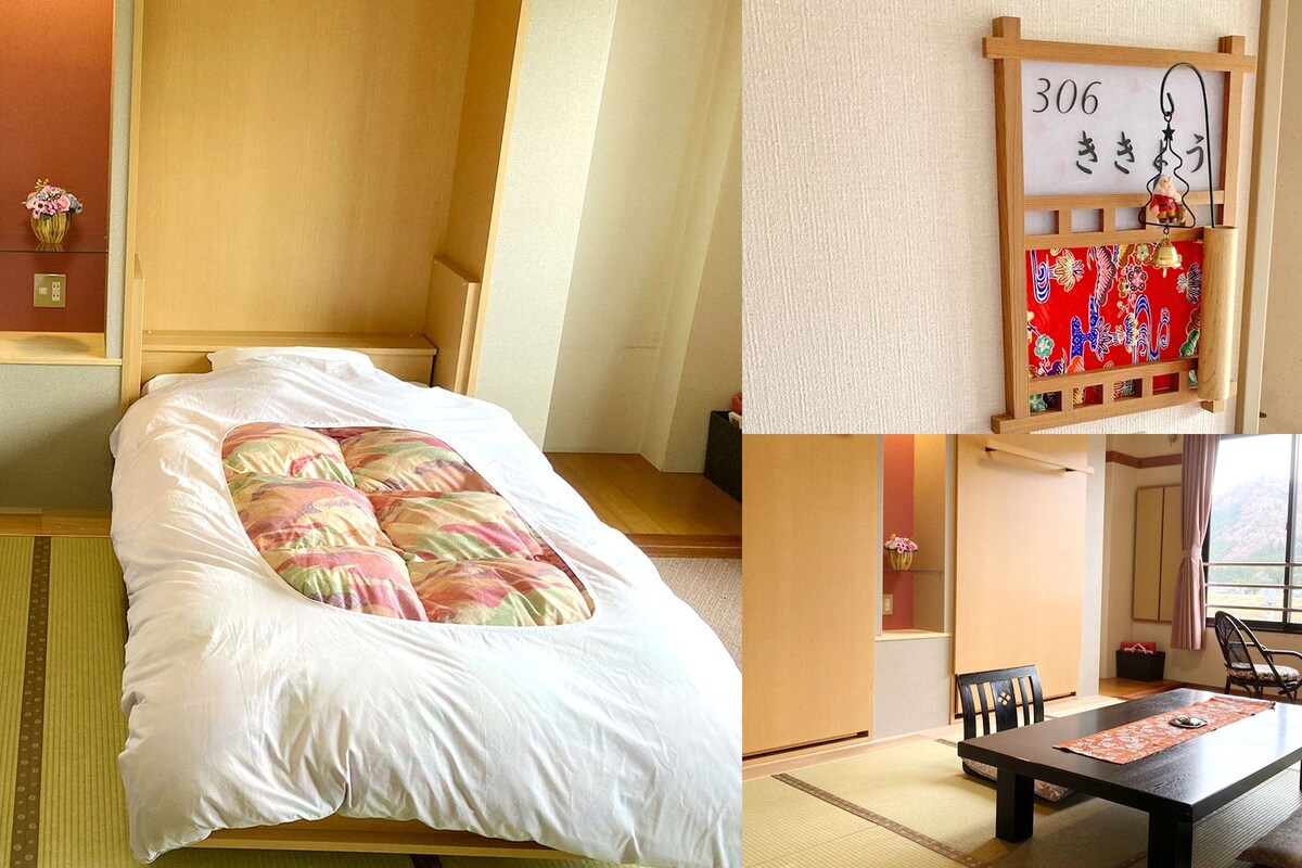 A room with two beds, a small table, chairs, a wall-mounted clock, and a view of the outdoors.