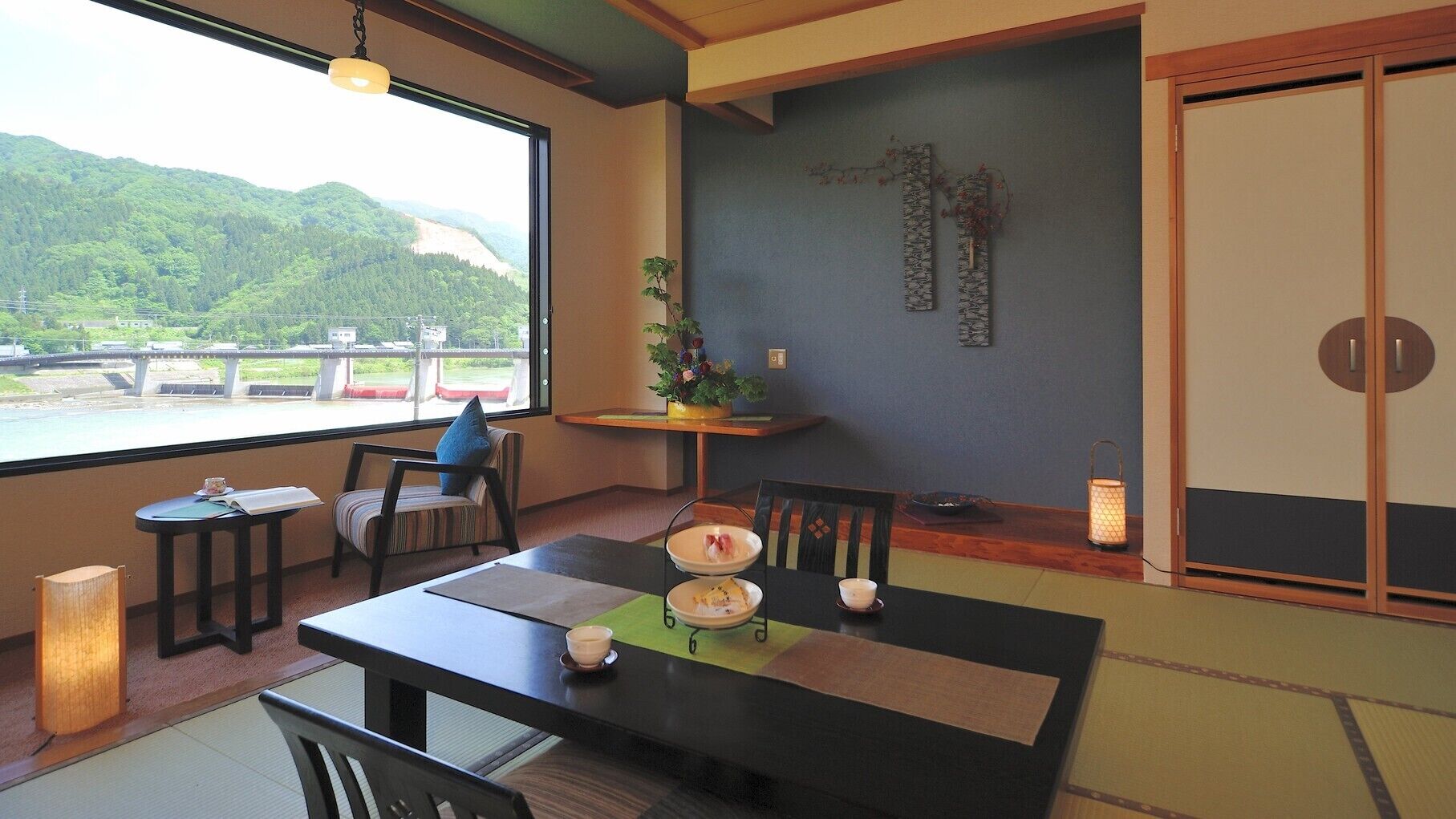 A dining area with a view of a bridge and hills, a table with plates and bowls, a chair with a blue cushion, and a hanging light fixture.