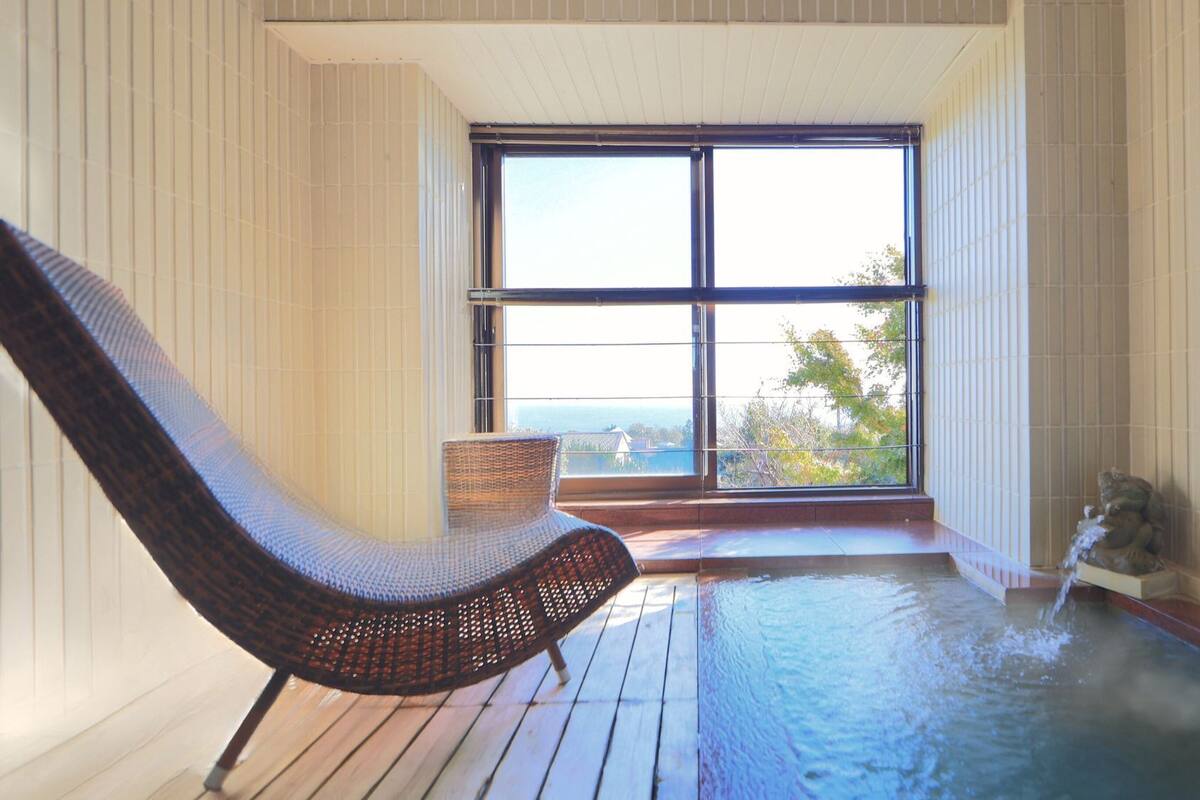 Un espace spa comprenant un bain à remous, un fauteuil en osier et une vue dégagée sur l’extérieur grâce à une grande fenêtre.