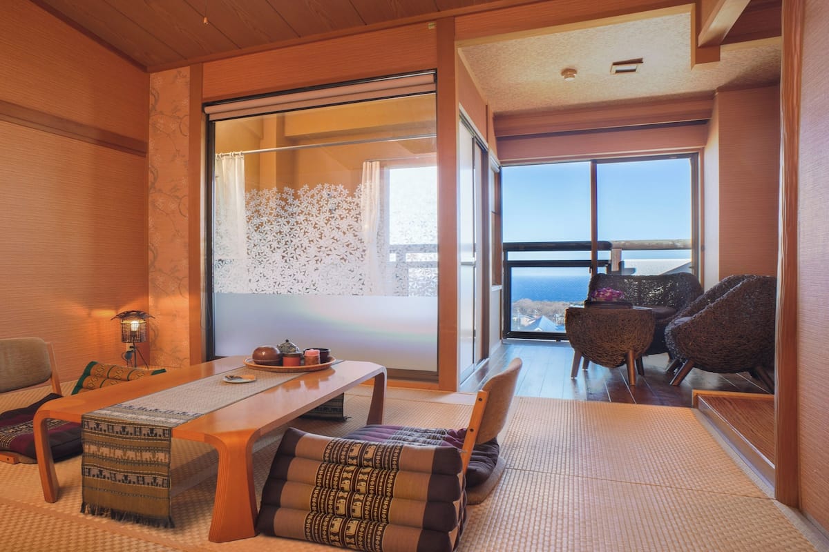 A traditional Japanese-style room with tatami flooring, a low table, and a view of the sea through large windows.