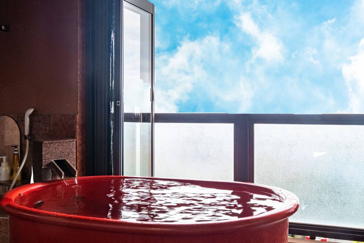 Une baignoire rouge donnant sur le ciel par une fenêtre.