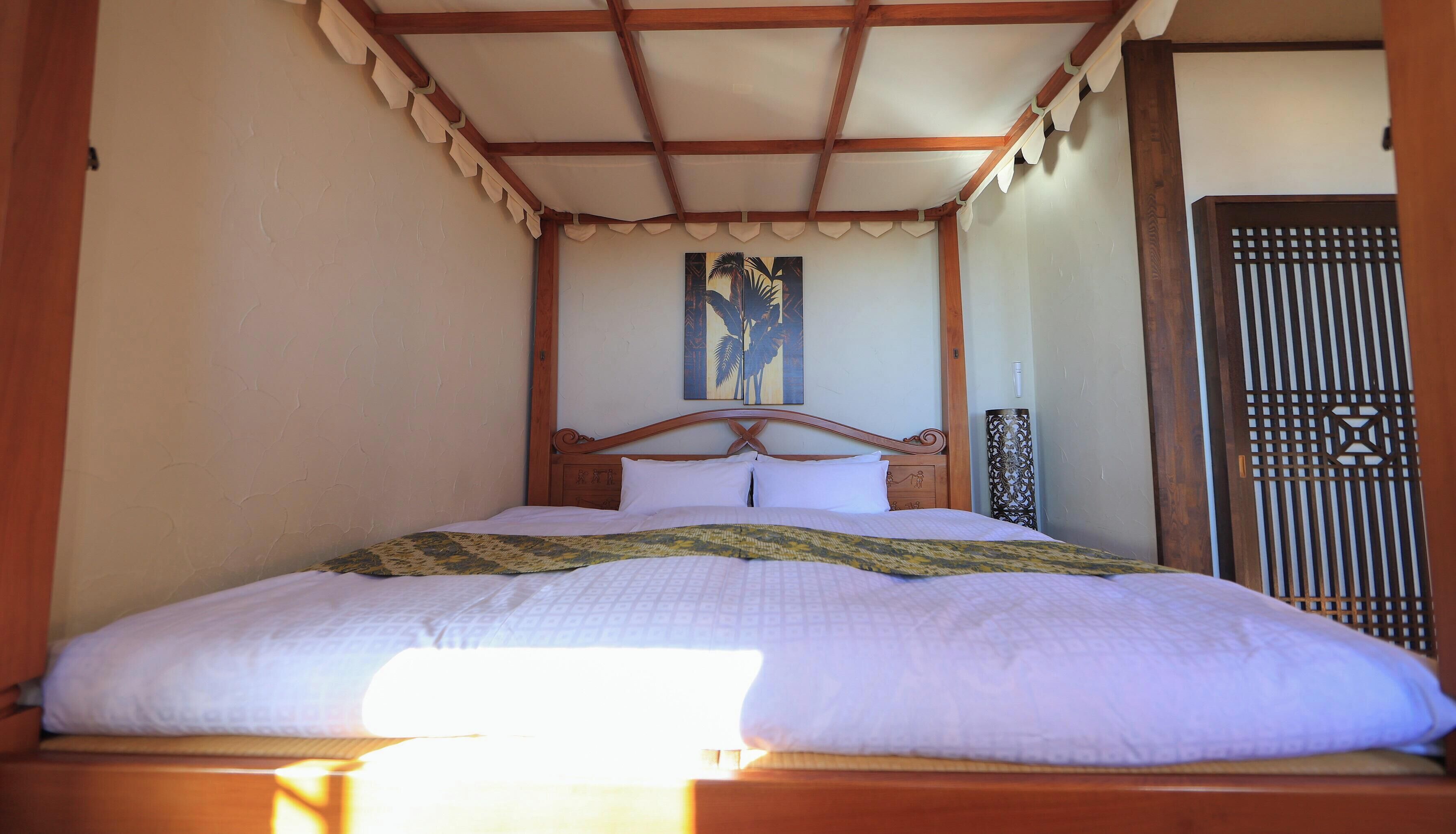Una cama con cabecera de madera, colcha estampada y un cuadro sobre la cama.