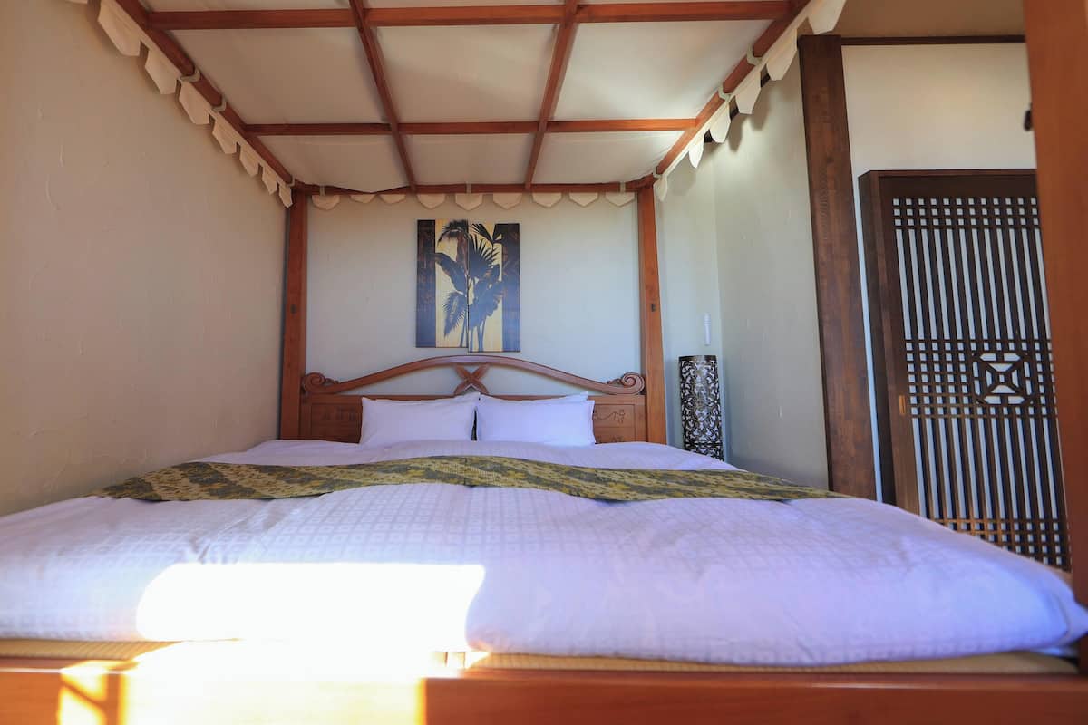 A bed with a wooden headboard, a patterned bedspread, and a painting above the bed.