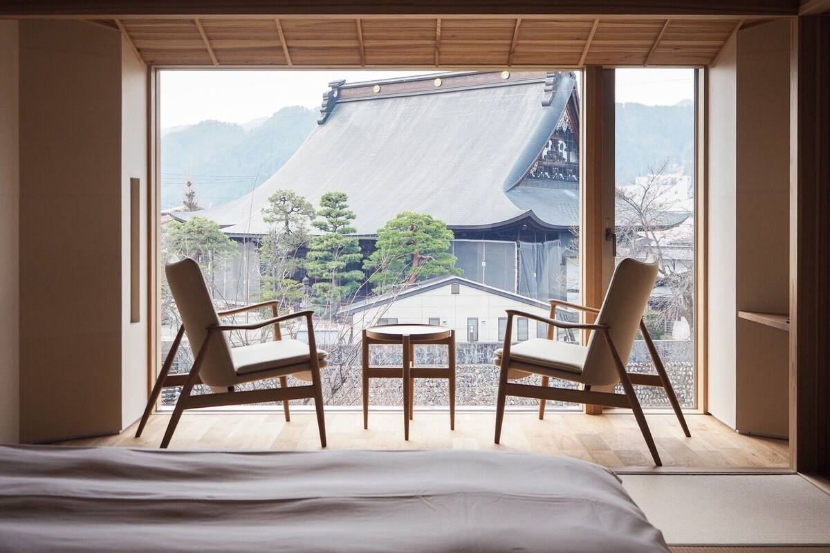 Une chambre avec un lit, deux chaises, une petite table et une vue sur une architecture traditionnelle.