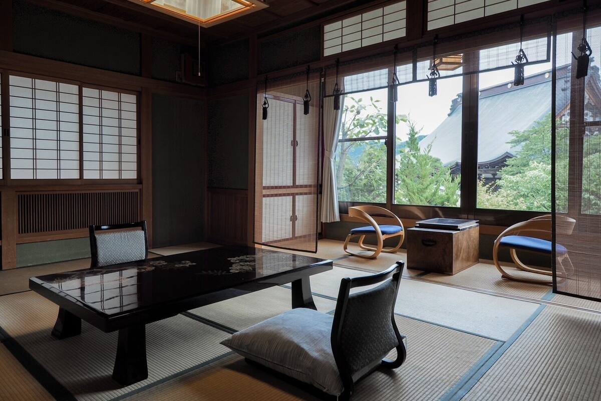 Une pièce de style japonais traditionnel, avec un sol recouvert de tatamis, une table basse et une vue sur la verdure environnante.