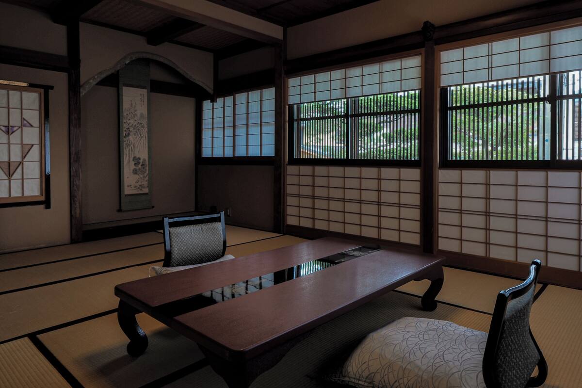 Une pièce traditionnelle avec un sol recouvert de tatamis, une petite table, deux chaises et des paravents en papier de riz (shoji).