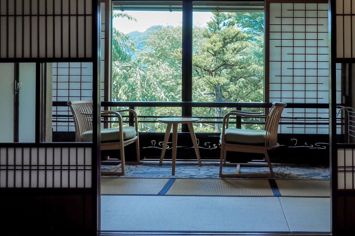 Une pièce de style japonais traditionnel, avec un sol recouvert de tatamis, une porte coulissante et une vue sur une végétation luxuriante.