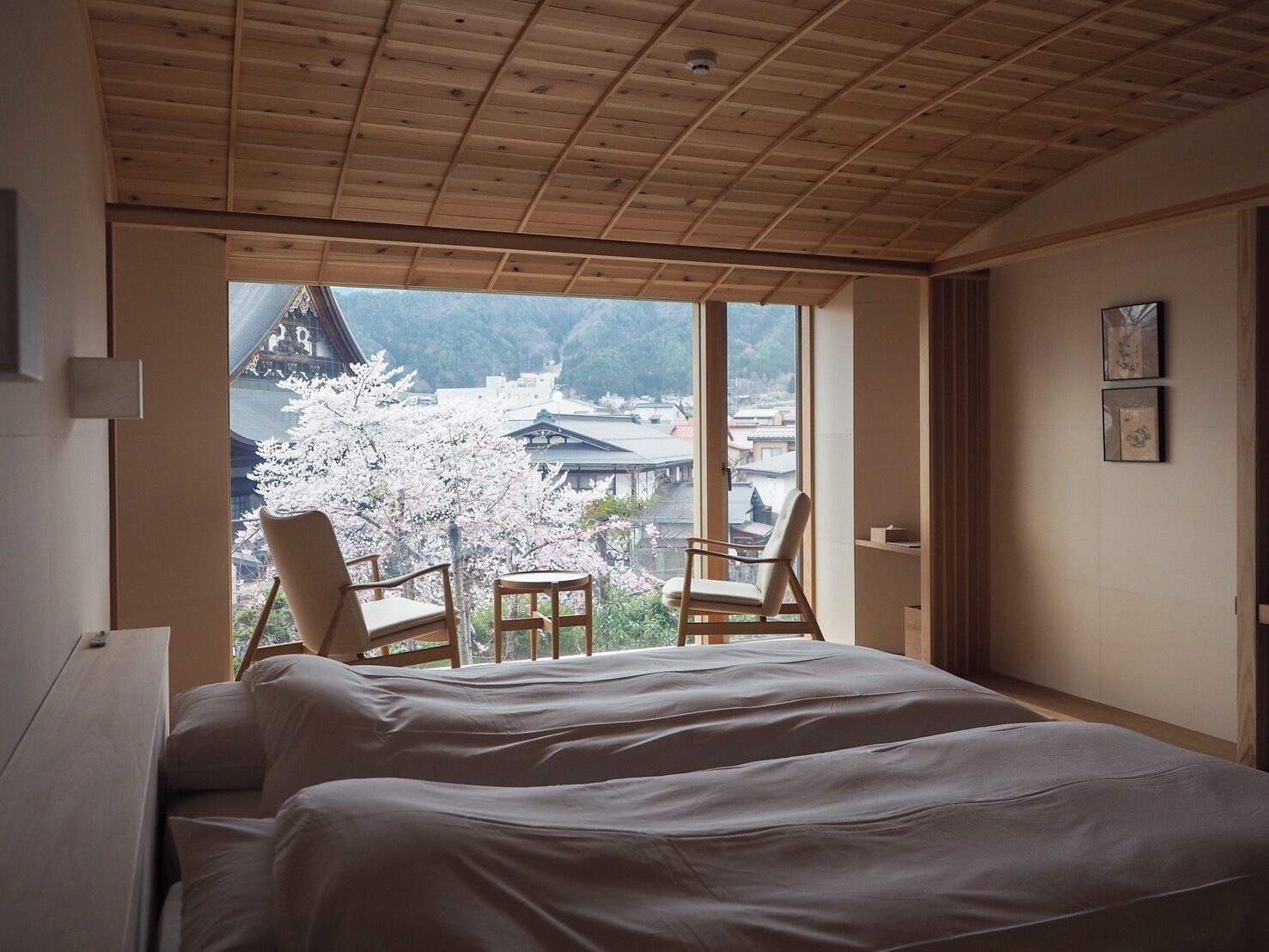 Un dormitorio con una cama grande, dos sillas y vistas a flores de cerezo, con arquitectura tradicional fuera de la ventana.