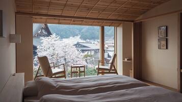 Un dormitorio con una cama grande, dos sillas y vistas a flores de cerezo, con arquitectura tradicional fuera de la ventana.