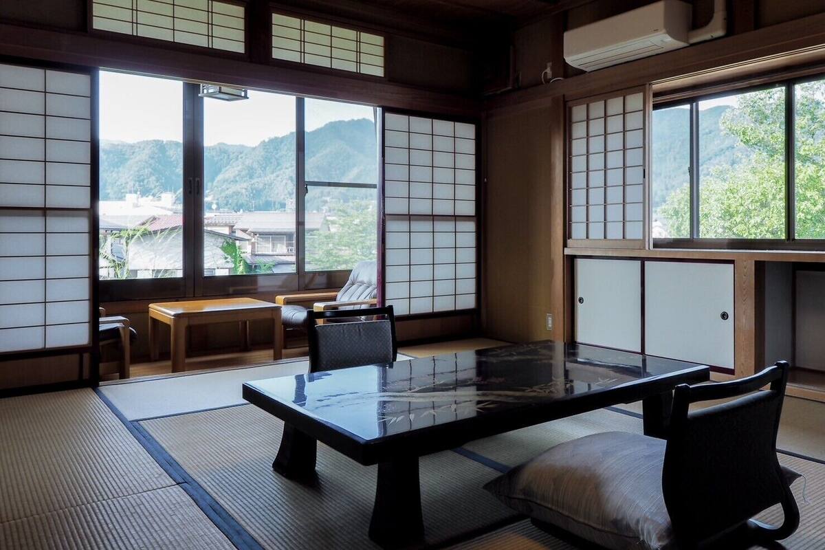 Une pièce de style japonais traditionnel, avec un sol recouvert de tatamis, une table basse et une vue sur un paysage montagneux.