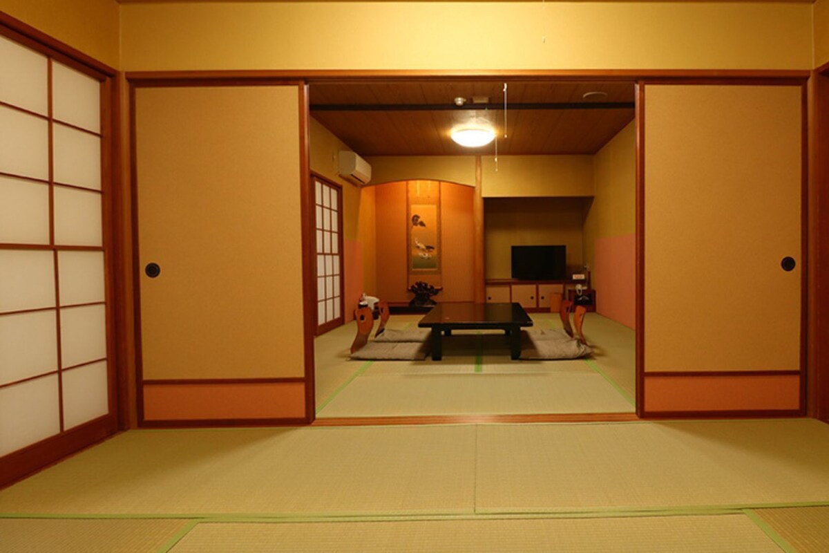 A traditional Japanese room with tatami flooring, sliding doors, a low table, and a television.