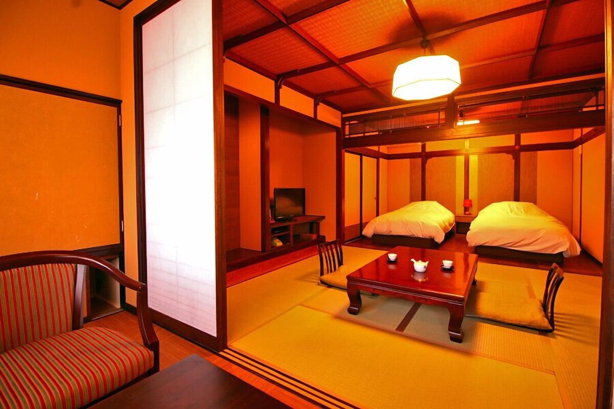 A traditional Japanese room with tatami flooring, a low table with a tea set, two beds, and a sliding door.