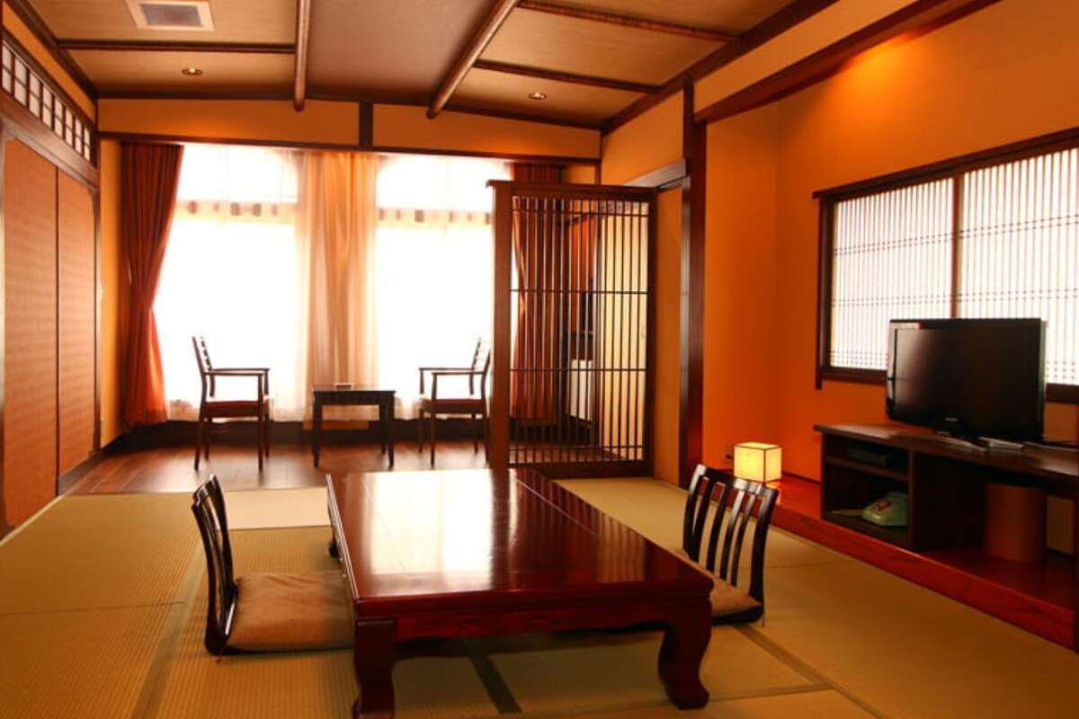 A traditional Japanese-style room with tatami flooring, a low table, chairs, a TV, and sliding doors.